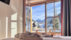 A bedroom with a large bed, a TV mounted on the wall, and a window with a mountain view. - FIRSTpeak (Altenmarkt im Pongau)
