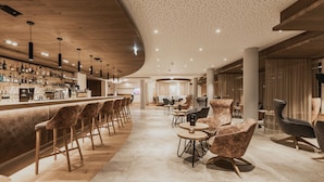 A modern bar area with a long counter, bar stools, and round tables with chairs. - FIRSTpeak (Altenmarkt im Pongau)