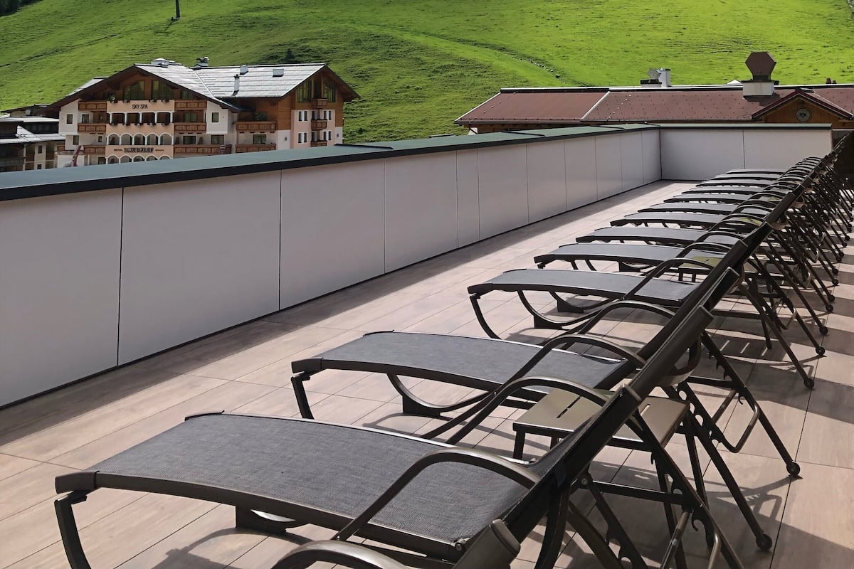 A terrace with outdoor seating and a view of a green hill and a building with a sign that reads "HOTEL SPA".