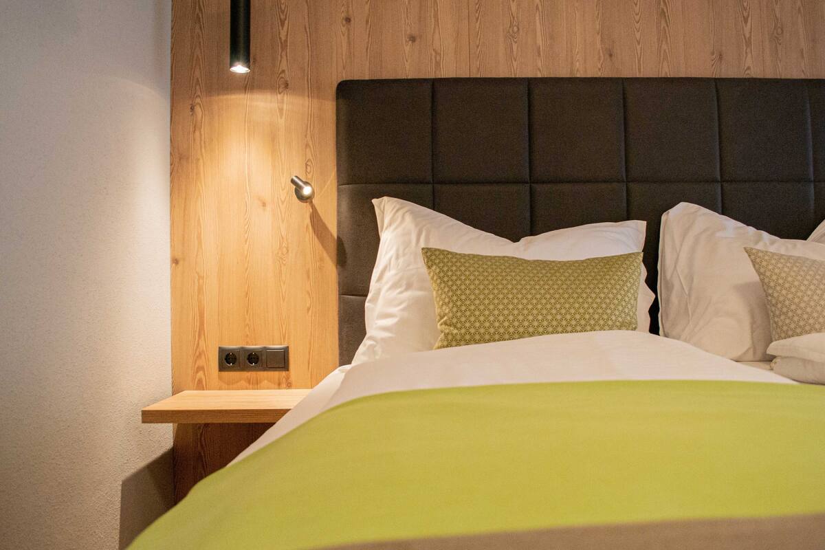 A hotel room with a wooden headboard, a bedside table with a lamp, and a bed with a green bedspread.