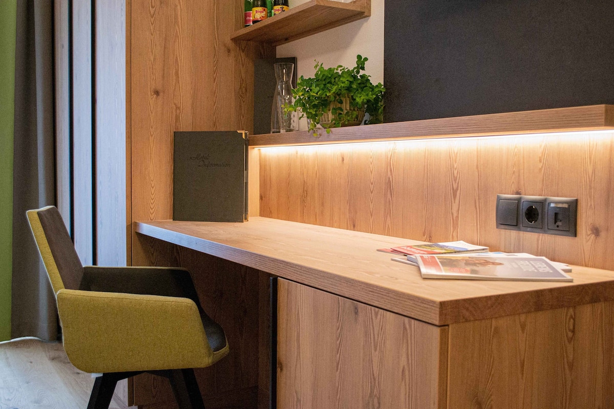A wooden desk with a chair, a plant, and a magazine on it.
