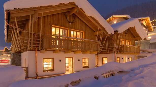 A wooden chalet with a balcony, snow-covered roof, and illuminated windows. - FIRSTpeak (Altenmarkt im Pongau)