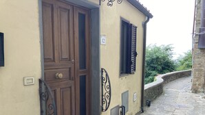 Un edificio con puerta de madera, ventana con contraventanas, pared de piedra y calle pavimentada.