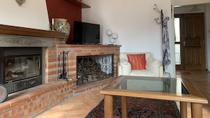 Una sala de estar con chimenea de ladrillo, televisor, sofá y mesa de centro de vidrio.