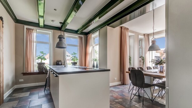 Una cocina moderna con una isla central, ventanas amplias y un comedor con sillas.