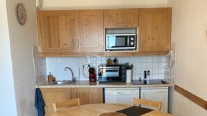 A compact kitchen with wooden cabinets, a microwave, a toaster, and a sink. There is a round wooden table with chairs and a black placemat. - Magnificent 6-person apartment 50 m from the slopes Household linen and towels included! (Valmeinier 1900)