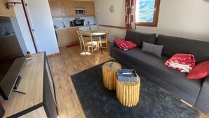 A compact living space with a kitchenette, a dining area, and a seating area with a sofa and two round wooden side tables. - Magnificent 6-person apartment 50 m from the slopes Household linen and towels included! (Valmeinier 1900)