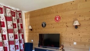 A cozy living room with a wooden wall, a TV, a blue sofa, and a patterned curtain. - Magnificent 6-person apartment 50 m from the slopes Household linen and towels included! (Valmeinier 1900)