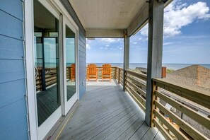 A wooden deck with a view of the ocean, a covered area with chairs, and a glass door leading inside. - Dune it Wright | Private Pool, Hot Tub | Oceanfront (Nags Head)