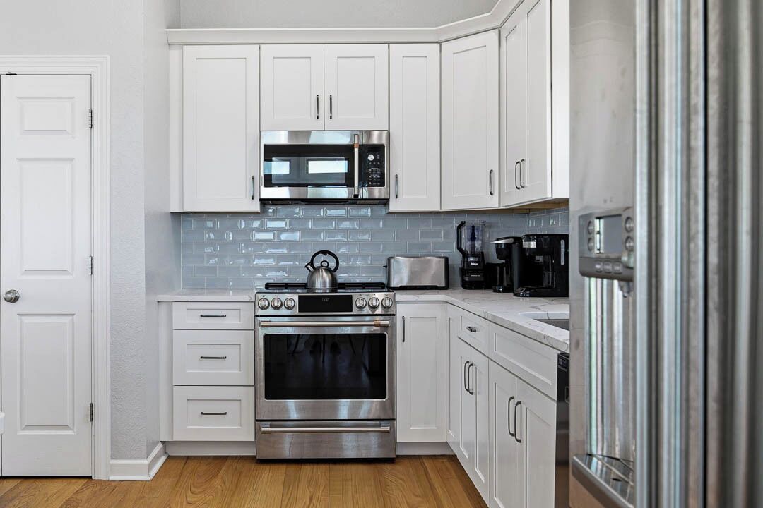 A modern kitchen with white cabinets, a stainless steel oven, a microwave, and a toaster.