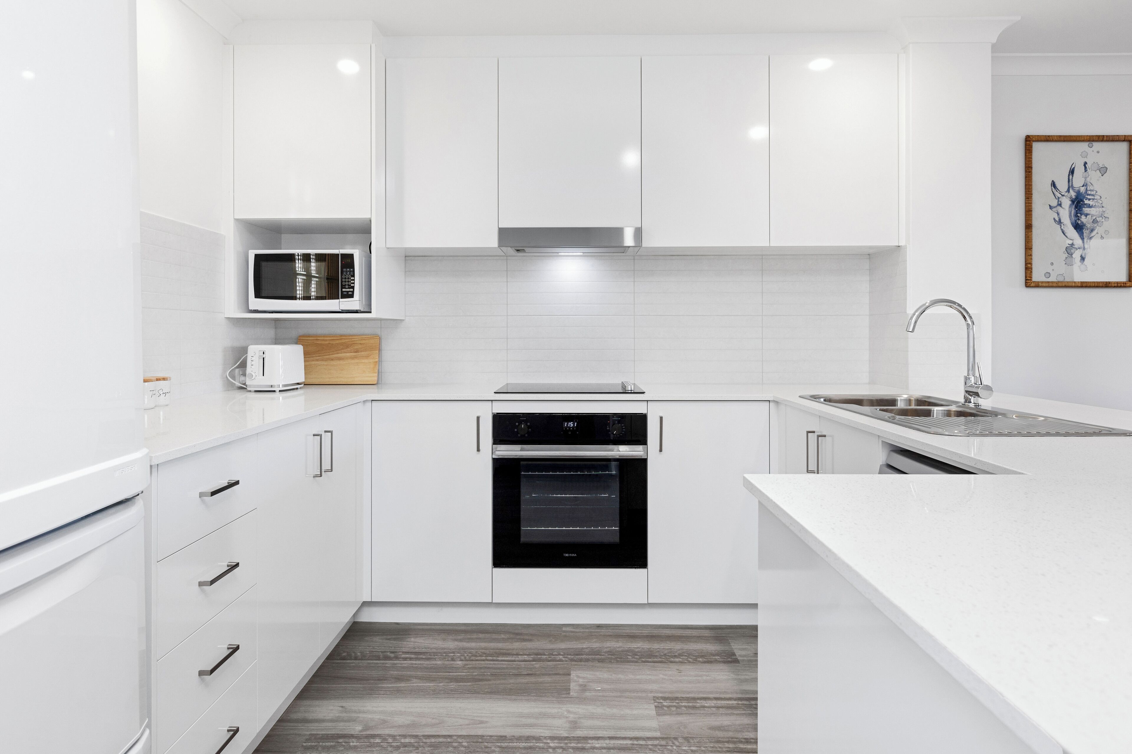 Una cocina moderna con armarios blancos, microondas, tostadora, estufa y lavaplatos.