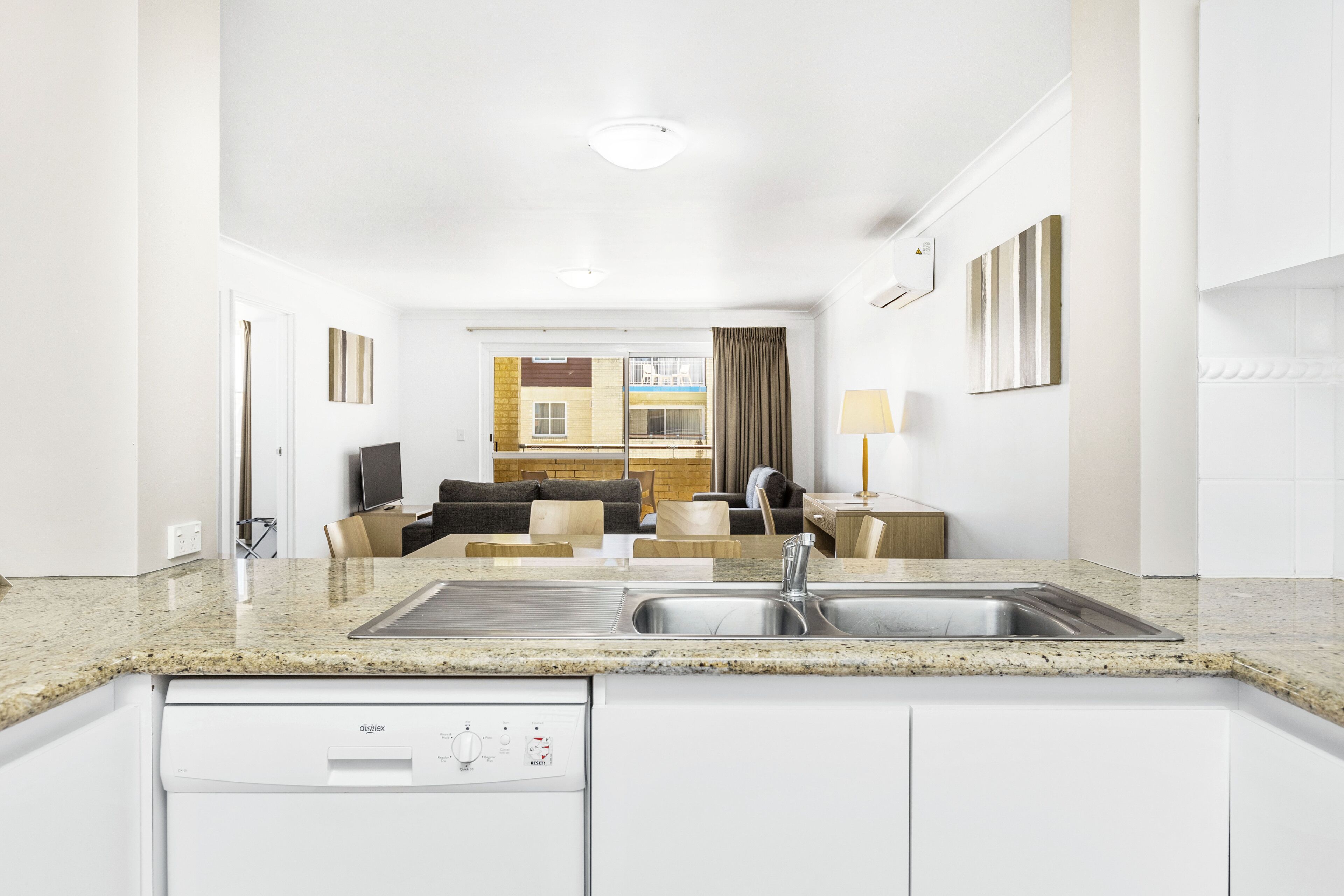 A modern kitchen with a dishwasher, double sink, and a dining area with a table and chairs.
