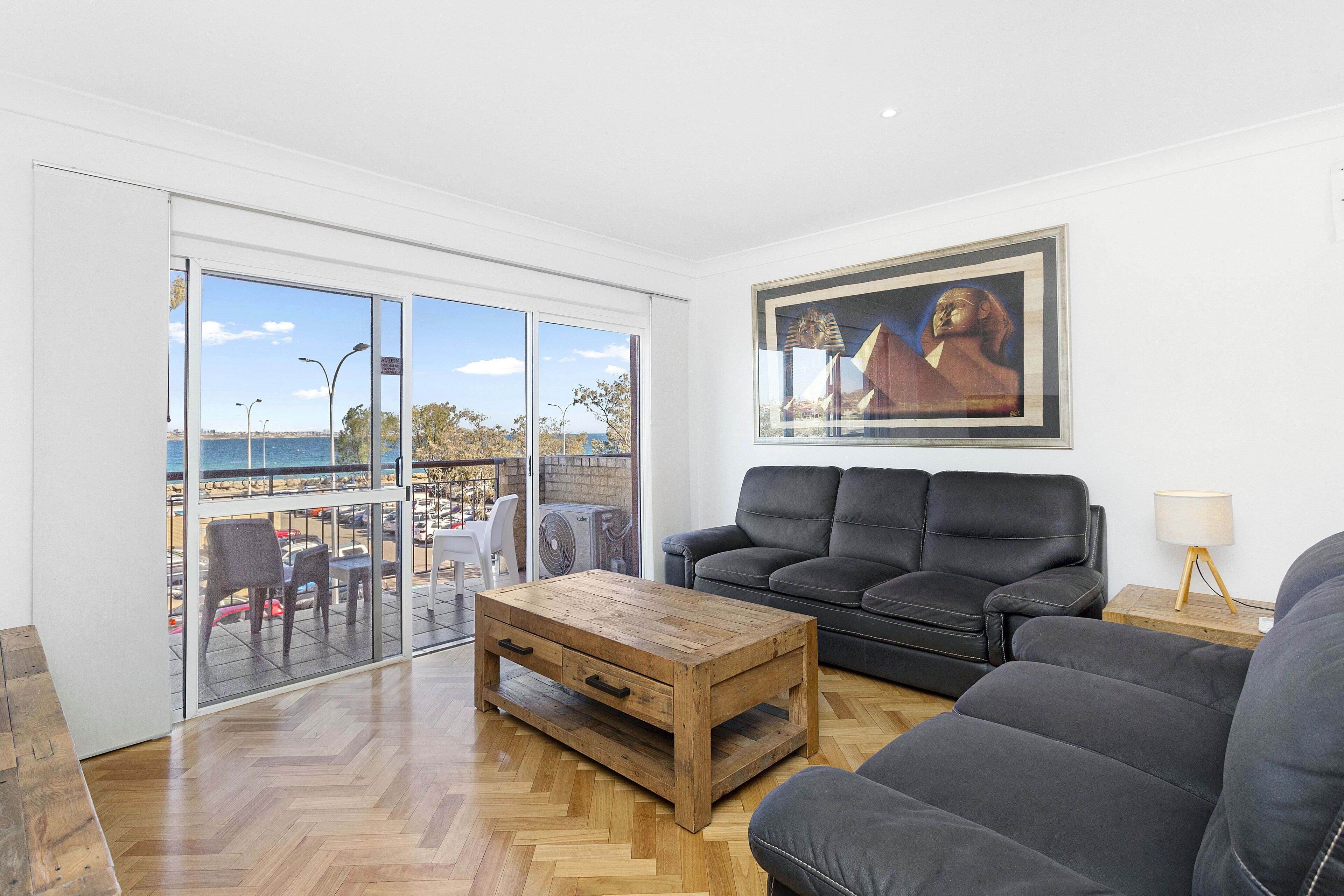 A living room with a wooden coffee table, a black leather sofa, and a painting of a historical figure.