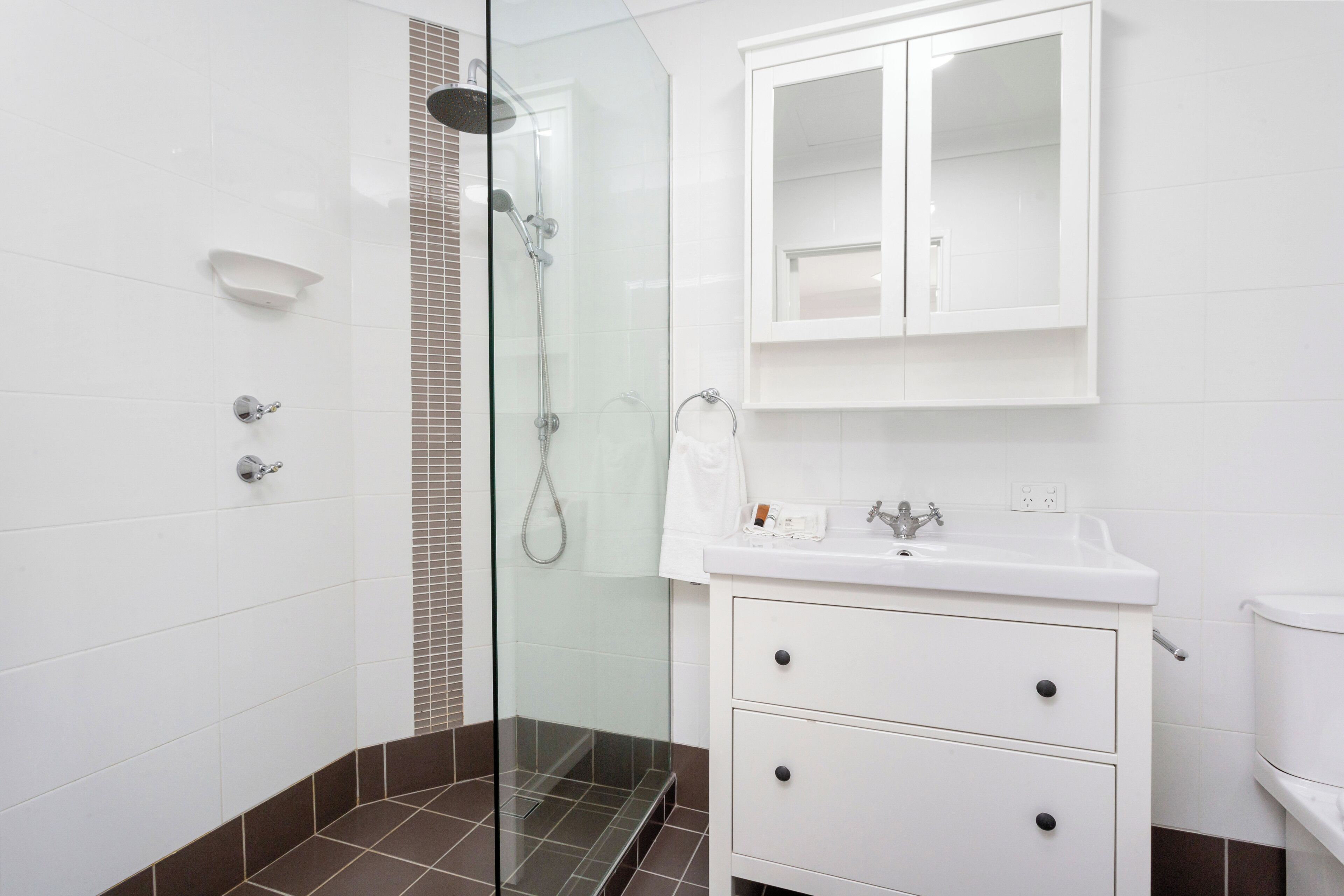 Un baño moderno con cabina de ducha de vidrio, tocador blanco con dos cajones y un inodoro blanco.