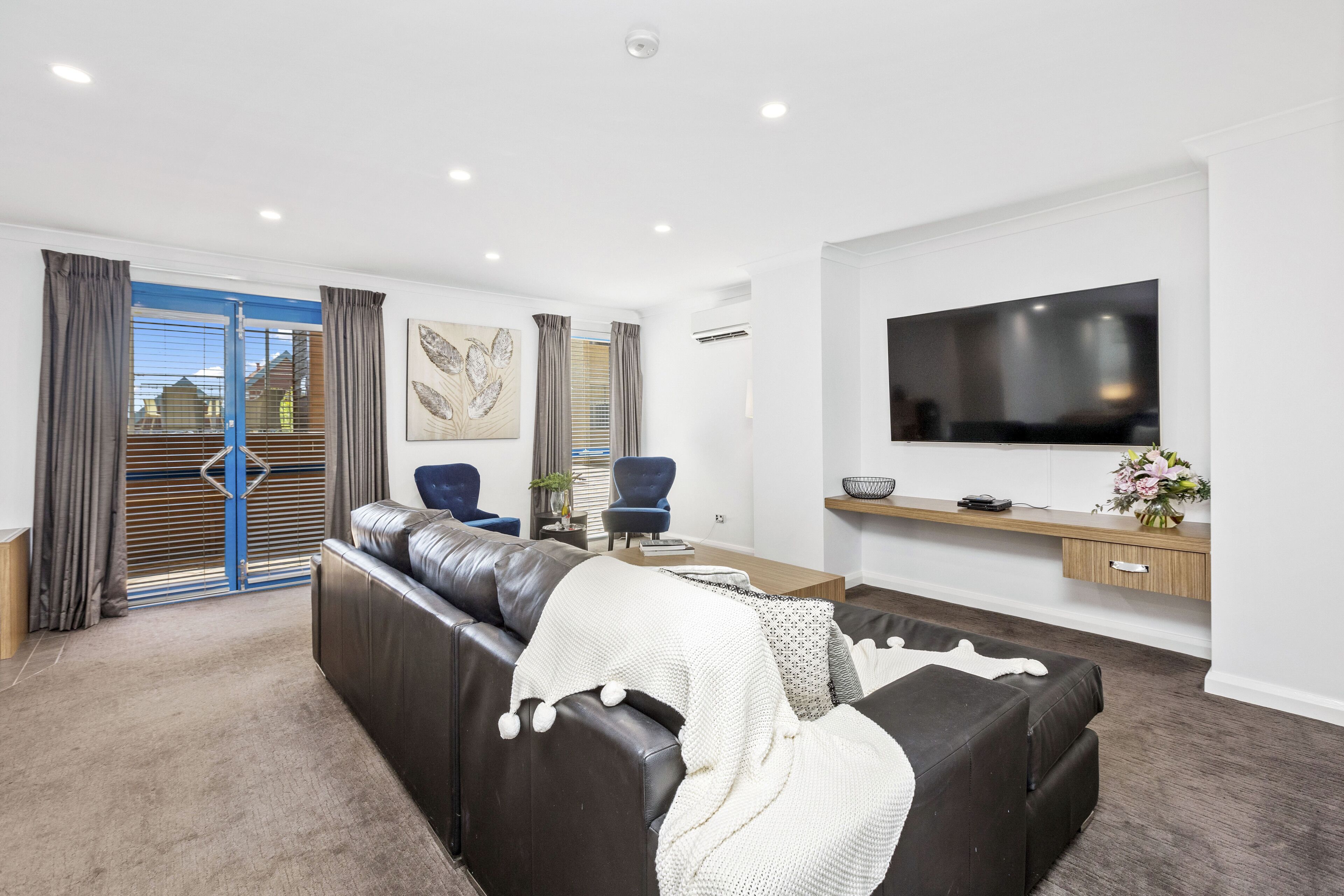 A modern living room with a leather sofa, a flat-screen TV mounted on the wall, and a sliding glass door leading to an outdoor area.