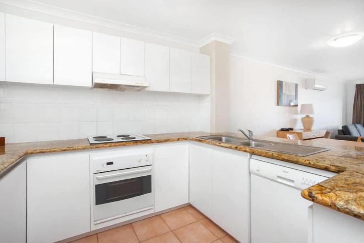 A modern kitchen with white cabinetry, a granite countertop, a built-in oven, and a dishwasher.