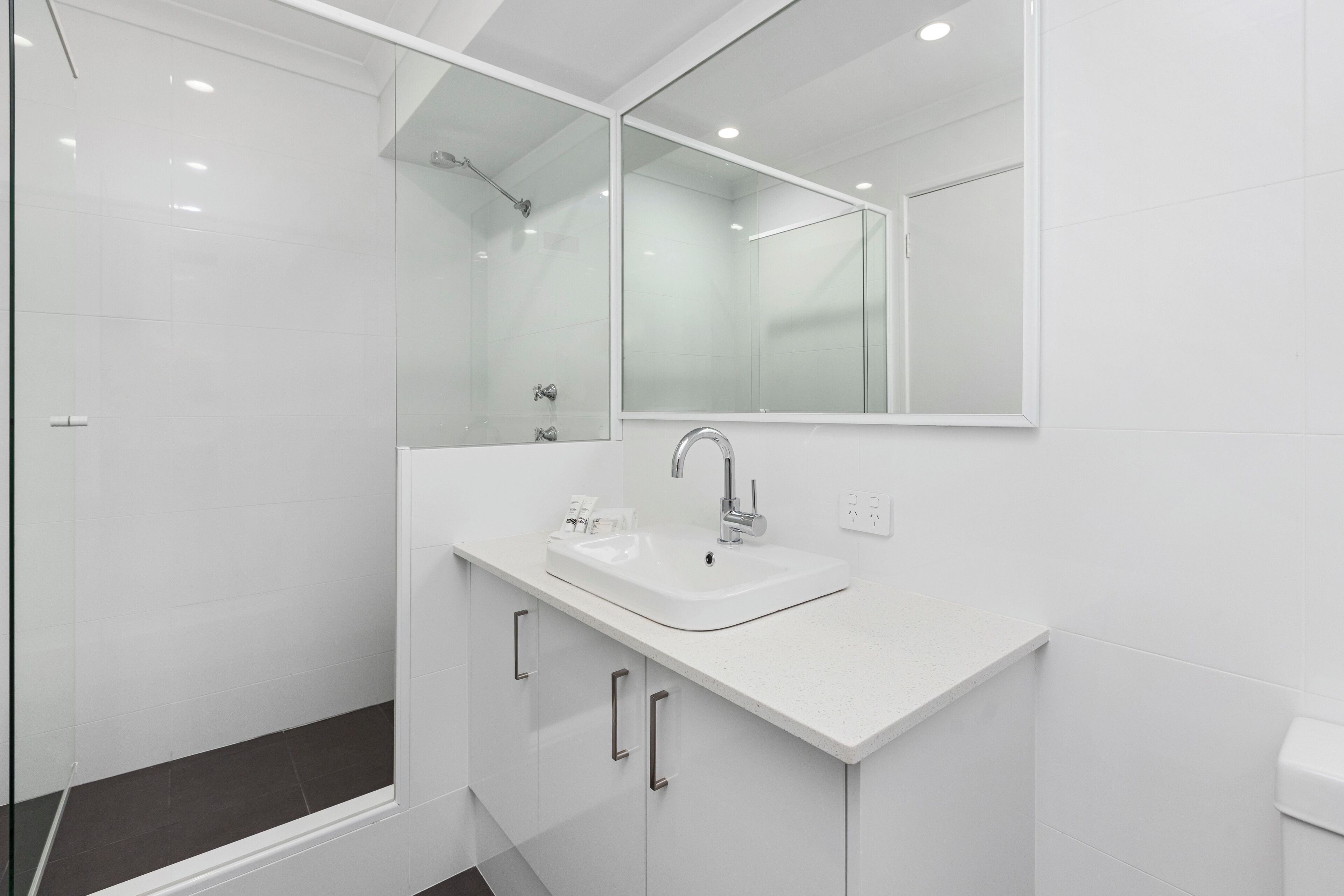 Une salle de bain moderne avec un lavabo blanc, un grand miroir et une douche à parois de verre.