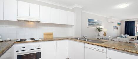 A modern kitchen with white cabinetry, a granite countertop, a built-in oven, and a dishwasher.