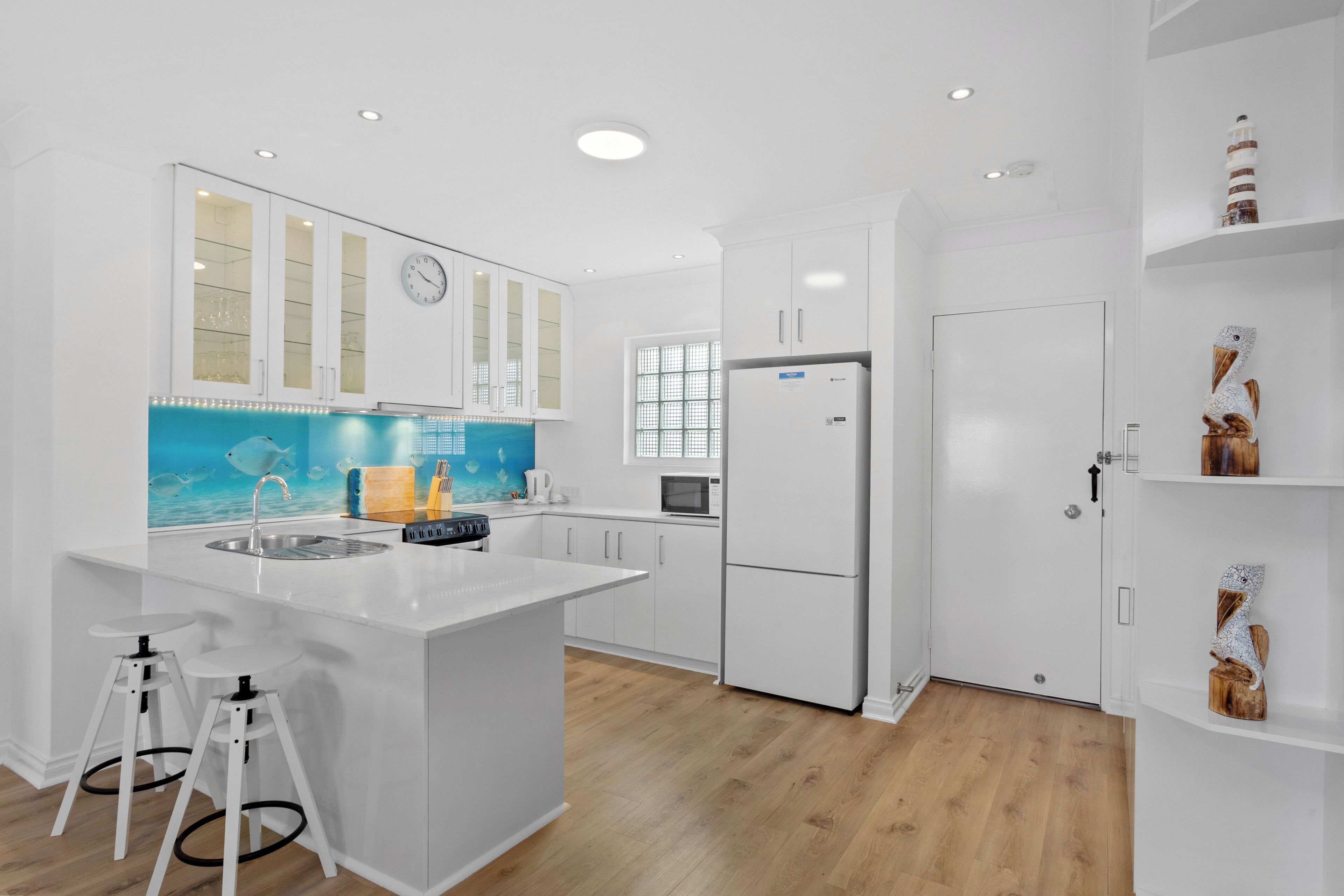 A modern kitchen with white cabinetry, a central island with stools, a microwave, and a refrigerator.