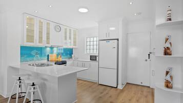 A modern kitchen with white cabinetry, a central island with stools, a microwave, and a refrigerator.