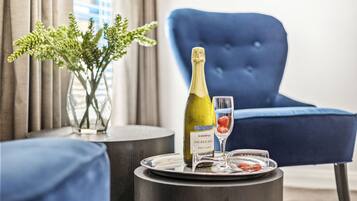 A bottle of wine on a tray with a glass, a vase with green plants, and a blue chair in a room.