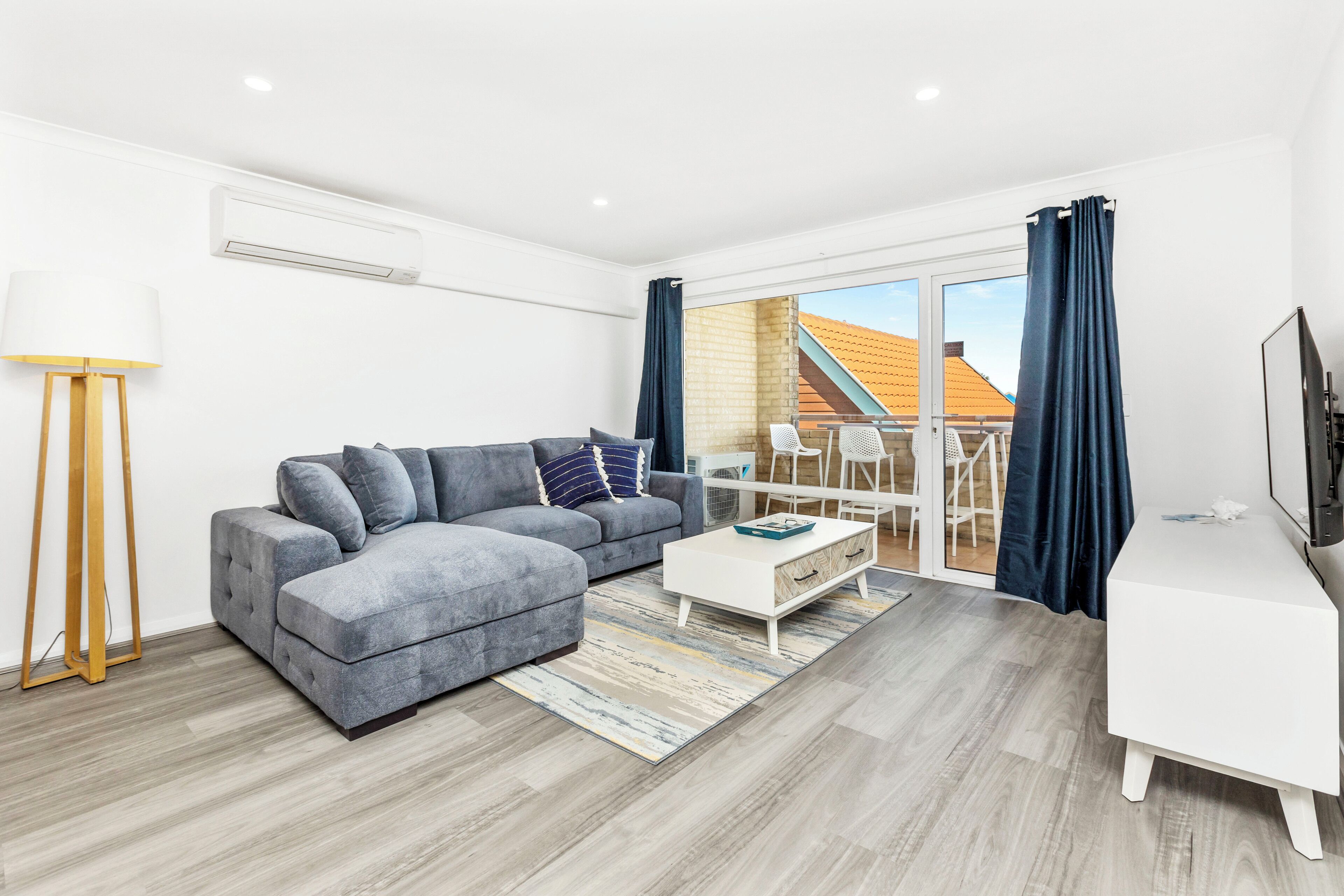 Una sala moderna con un sofá gris, una mesa de centro blanca y un mueble para televisión.
