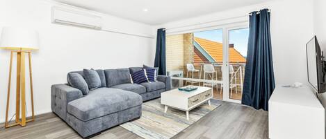 Una sala moderna con un sofá gris, una mesa de centro blanca y un mueble para televisión.