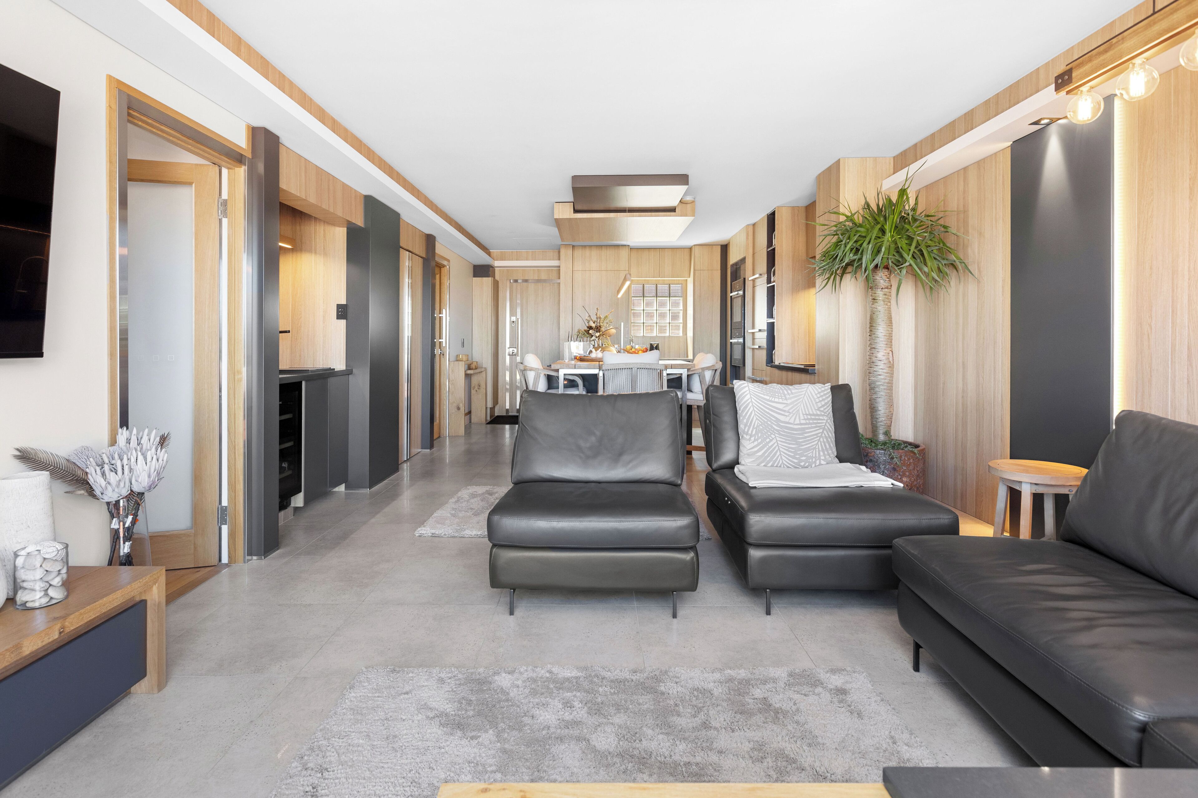 A modern living room with a sofa, two armchairs, a coffee table, and a dining area with a table and chairs.