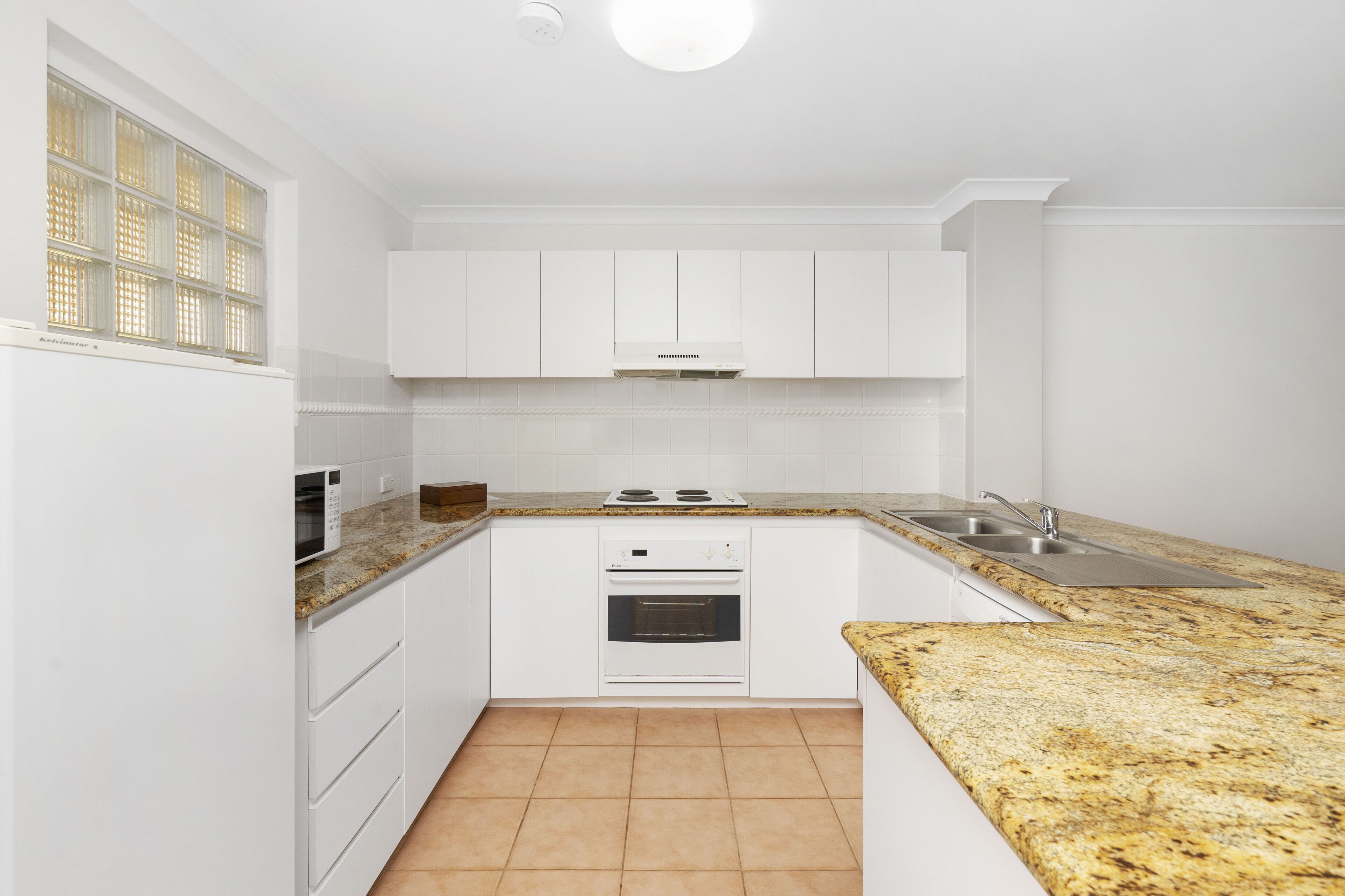 A modern kitchen with white cabinets, a granite countertop, a built-in oven, and a stainless steel sink.