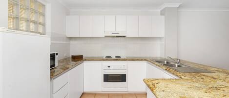 A modern kitchen with white cabinets, a granite countertop, a built-in oven, and a stainless steel sink.