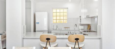 A modern kitchen with white cabinetry, a central island, and two bar stools.