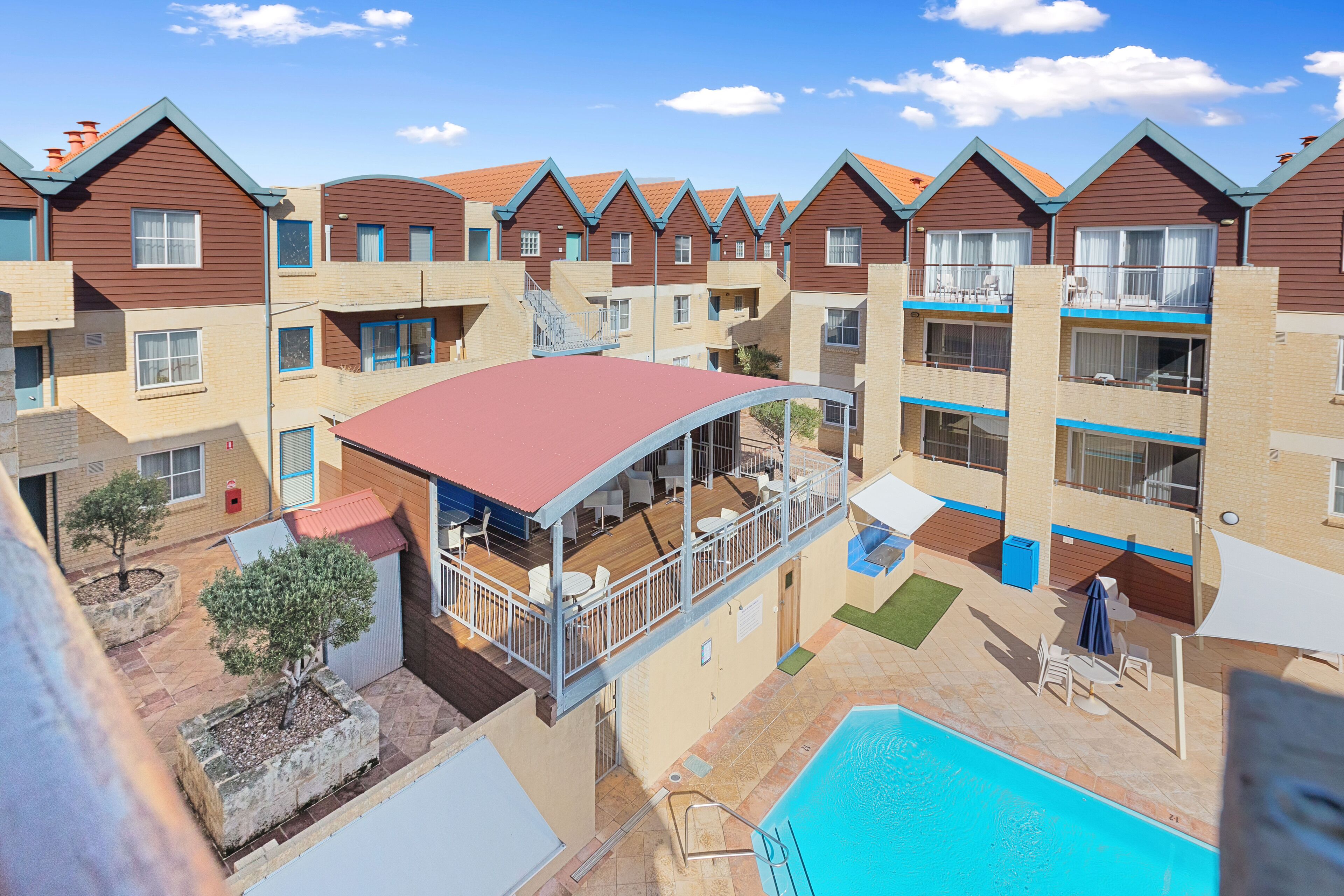 A residential building with multiple balconies, a swimming pool, and outdoor seating areas.