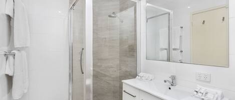 A modern bathroom with a glass-enclosed shower, a white sink, and a large mirror.