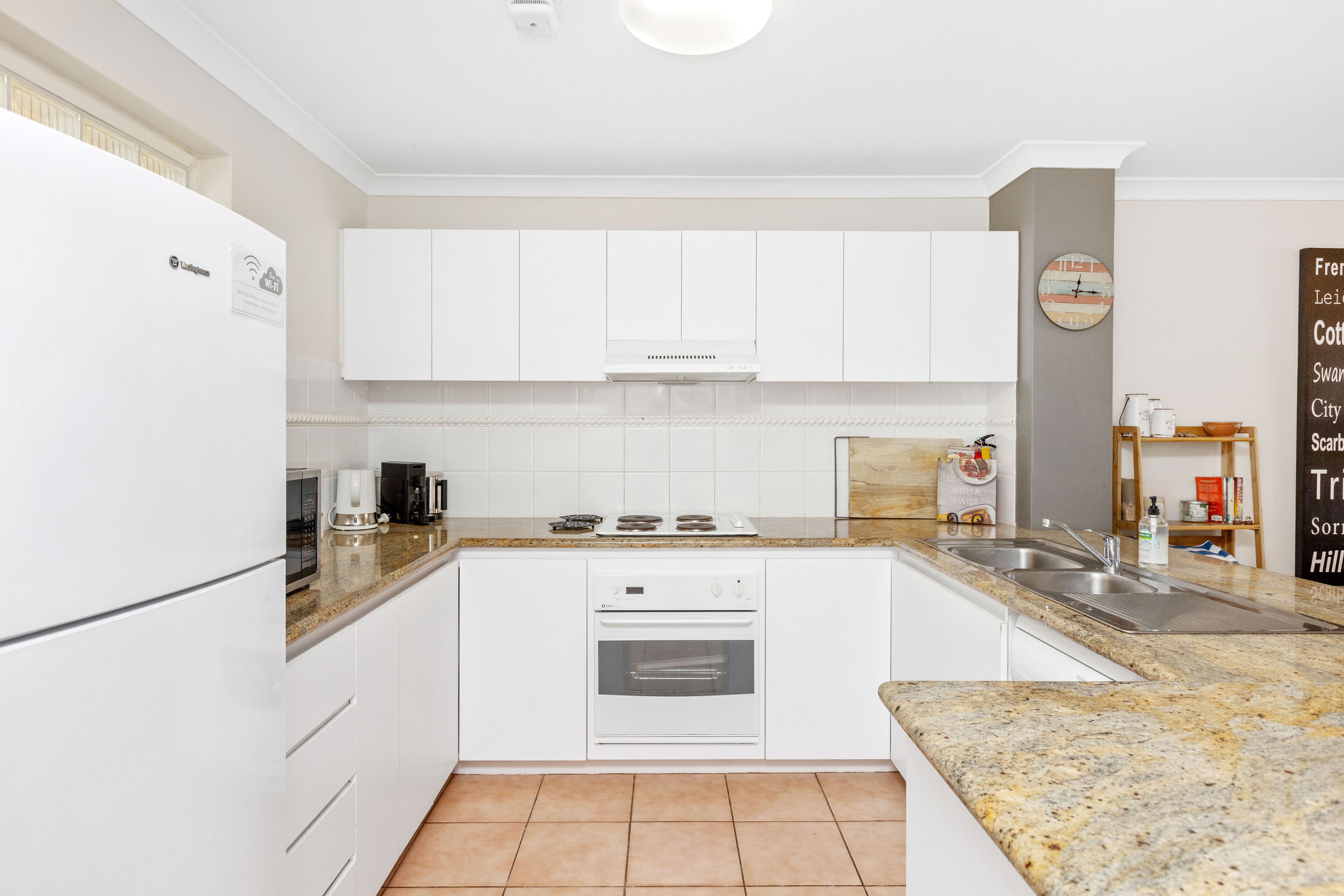 Een moderne keuken met witte kastjes, een granieten aanrechtblad, een inbouwoven en een roestvrijstalen spoelbak.