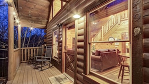 Een houten chalet met een veranda, een eethoek en een trap die zichtbaar is door een groot raam.