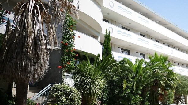 Um hotel com vários andares e varandas, cercado por palmeiras e vegetação.