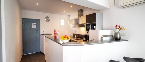A modern kitchen with a central island, bar stools, a clock, and a blue door.