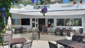 Um café ao ar livre com mesas e cadeiras, um letreiro com a inscrição "BISTRO ESTIVE" e vista para a rua.