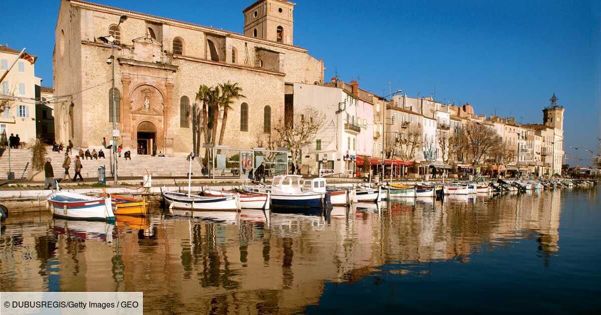 A waterfront with a historic building, boats docked along the shore, and a clear blue sky.