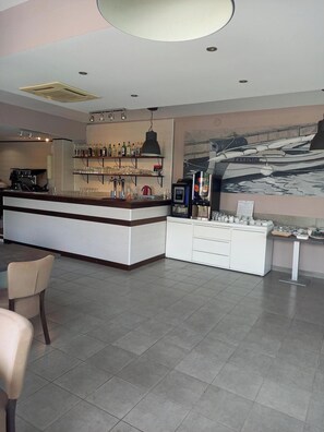 A modern bar area with a counter, shelves of bottles, glasses, and a coffee machine. There is a seating area with chairs and a table. - Residence le Saint Esteve (La Ciotat)