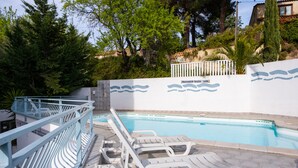 Piscina com cadeiras de descanso brancas e cercado branco com desenhos de ondas azuis.