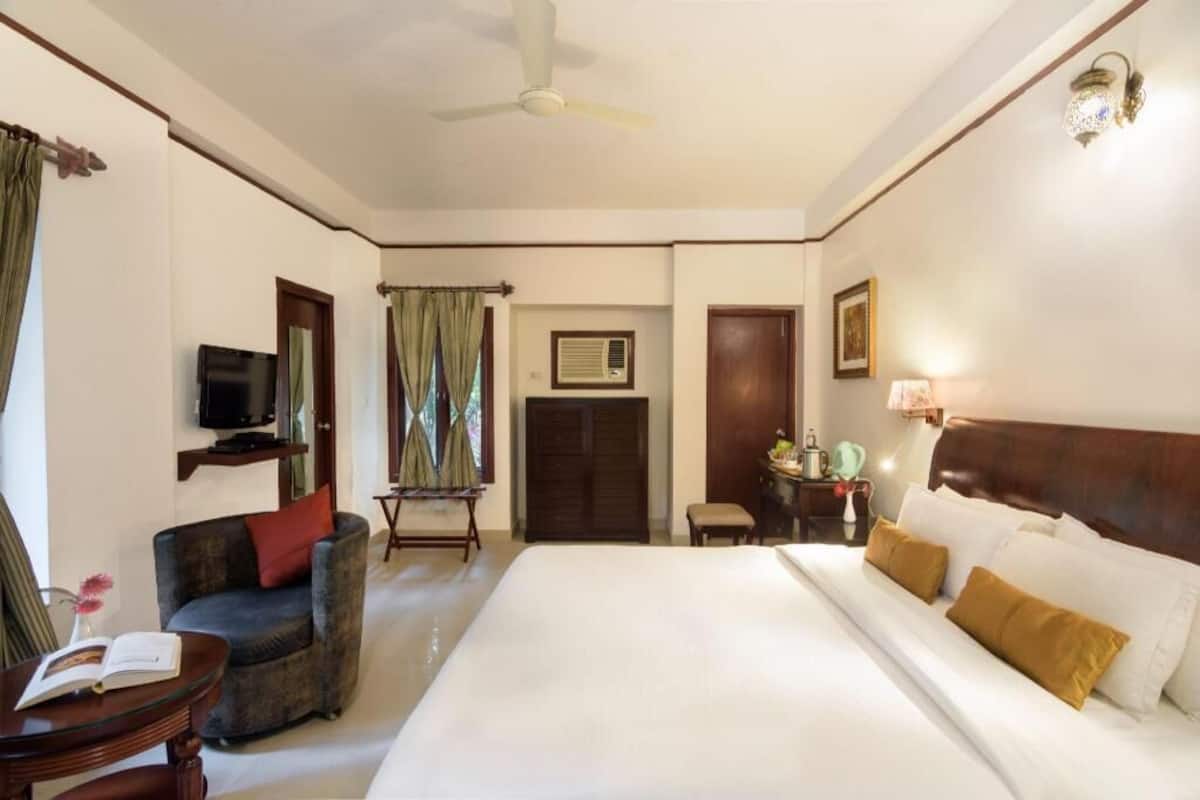 Una habitación de hotel con cama, televisión, silla, escritorio y ventilador de techo.