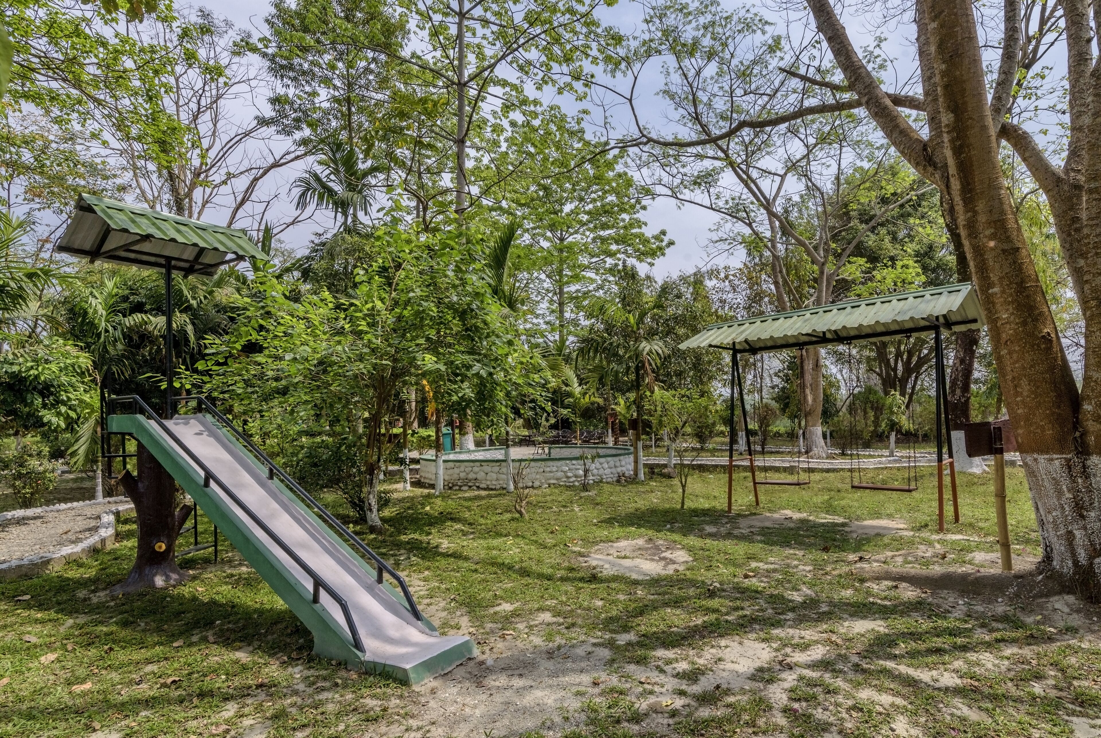 A playground with a slide and swings, surrounded by trees and greenery.