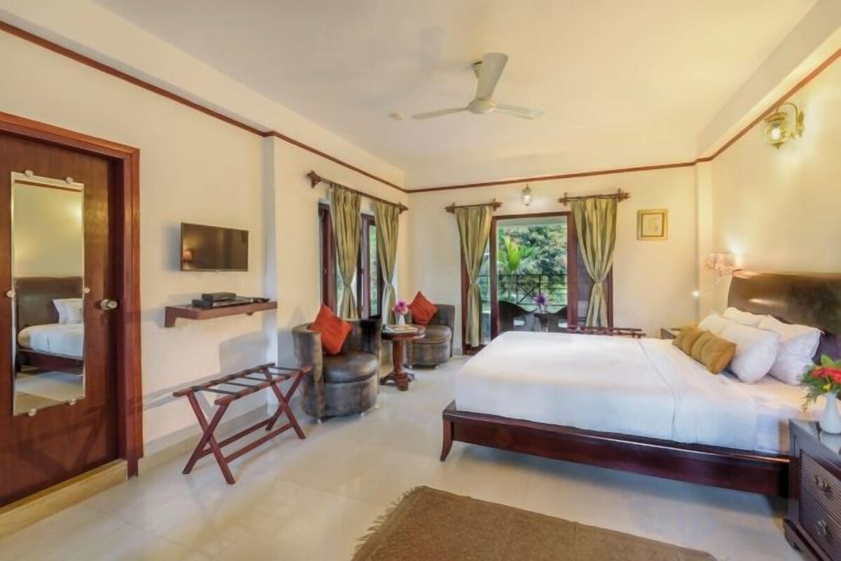 A bedroom with a bed, a TV, a chair, a small table, and a window with curtains.