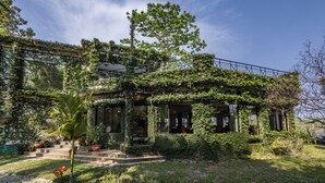A house with a covered porch, steps leading to the entrance, and a garden with various plants. - The Riverwood Forest Retreat - Dooars (Mal)