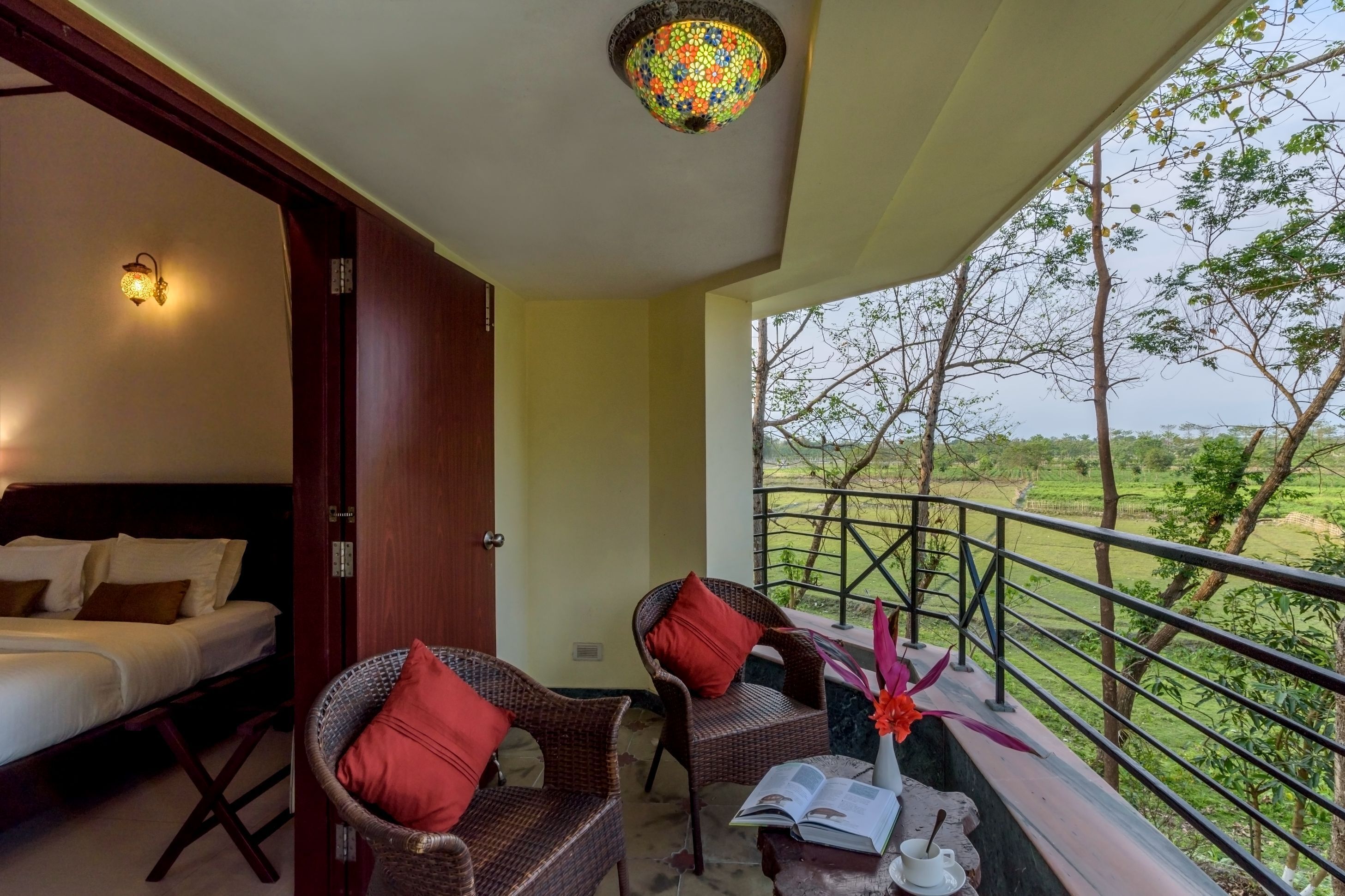 A balcony with wicker chairs, a small table with a book and a cup, and a view of a green landscape.