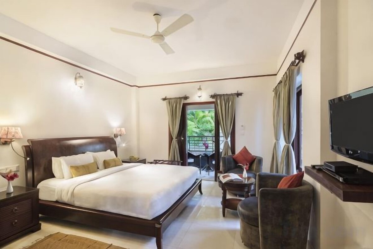 A bedroom with a bed, bedside table, lamp, TV, and a ceiling fan.