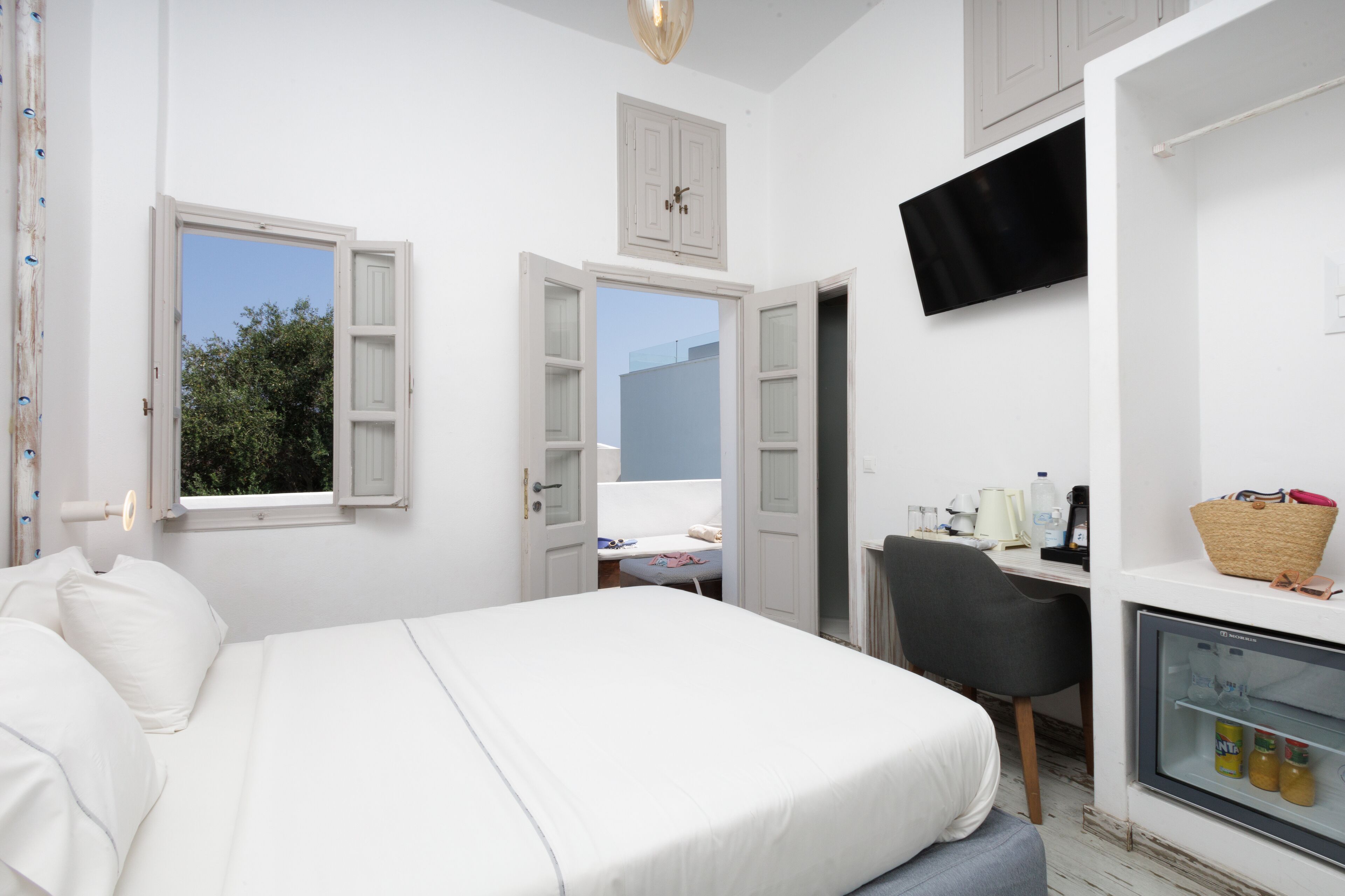 A bedroom with a bed, a desk, a chair, a TV, and a small refrigerator.