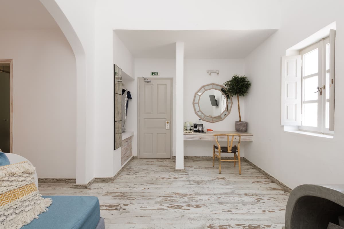 A room with a wooden floor, a desk with a mirror, a chair, and a bed with a blue blanket.