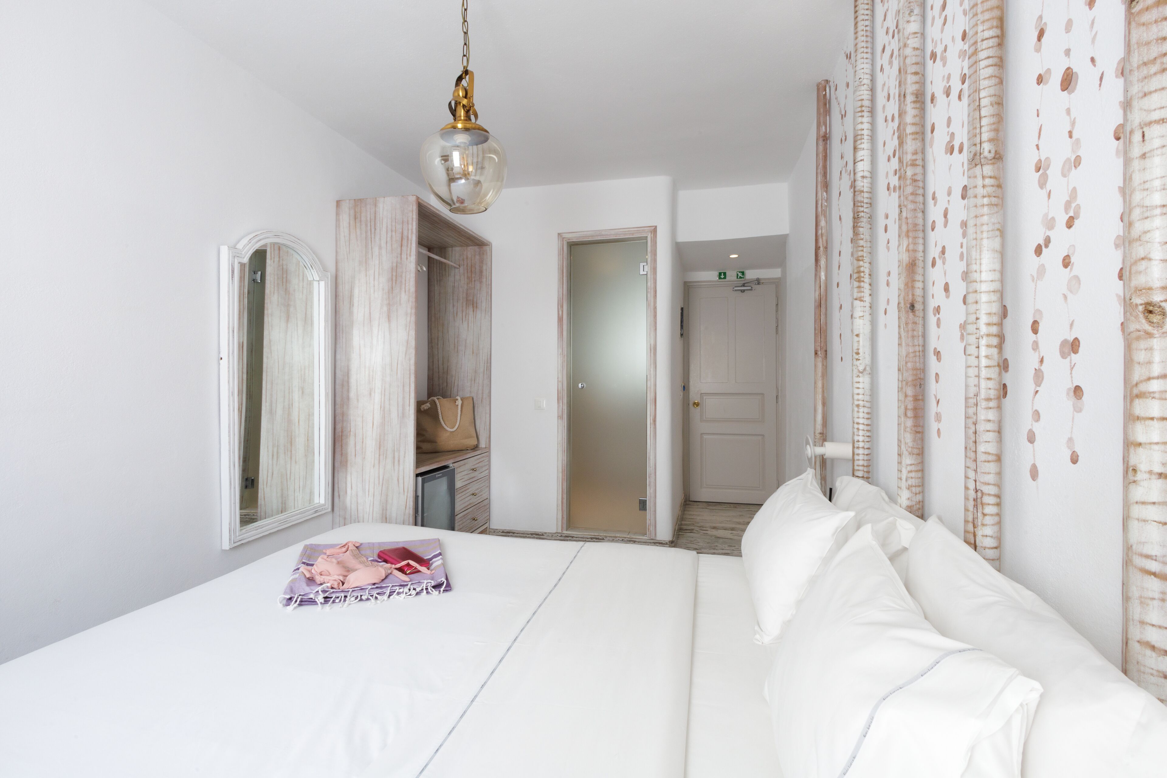 Une chambre à coucher comprenant un lit, une armoire, un miroir et un luminaire suspendu.